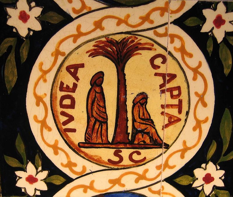 A white circle on a black background with green leaves and white flowers. Around the circle is a yellow vine border, and in the middle there is a palm tree. On the left side of the tree, an abstract figure in drapery stands, and on the right side, a similar figure sits.