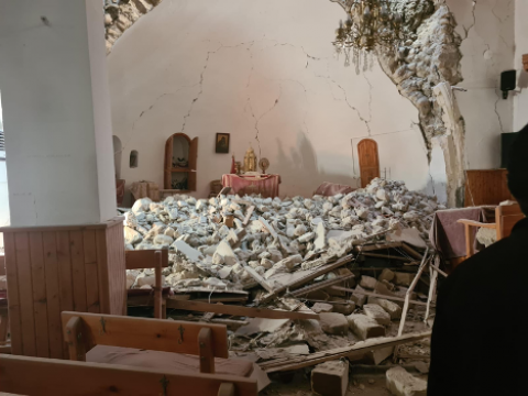 The inside of a church filled with debris and broken pews. An altar is still standing under an apse in the front.