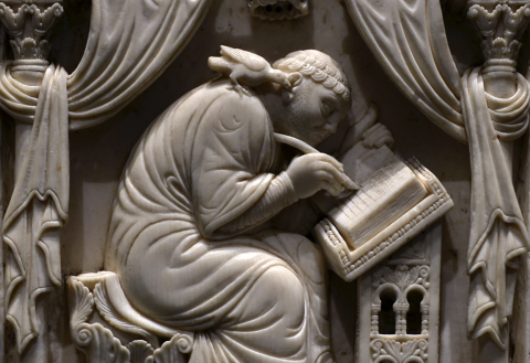 A stone relief of a figure seated above a desk, writing in a book