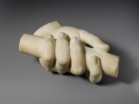 A white marble sculpture of a hand hold a long cylinder