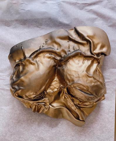 A golden breastplate of a woman's chest covered in drapery. A collarbone peeks out the top, and droplets of water trickle down.