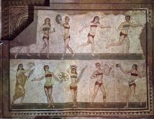 A mosaic featuring two rows of light-skinned women wearing brown bikinis. On top, two women are running, one hold a large object, and one stands still. On the bottom, one holds a crown, one holds a branch, and two play catch with a ball.