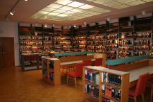 A large room with shelves of books lining the walls and wooden tables with red chairs and turquoise lamps across the middle