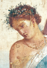 A section of a painted fresco showing a woman with auburn hair tied into a low bun. She wears a laurel crown and a turquoise toga over one shoulder, and she looks down to her right.