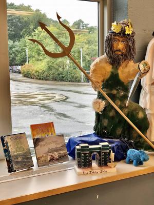 A window display featuring books about Greek myth, a model of the Ishtar Gate, and a large papier-mache figure of Poseidon.