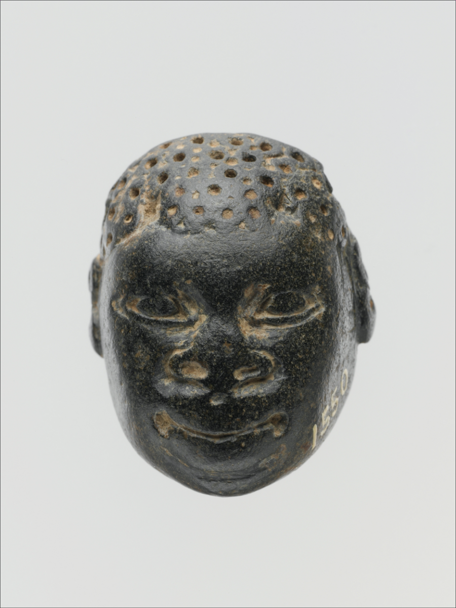 A black pendant shaped like a head, with a face carved into it and small holes on top to indicate hair.