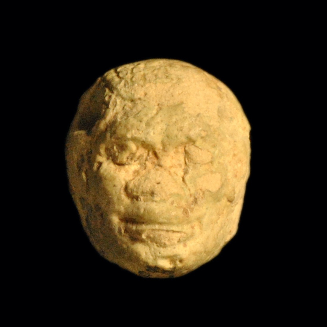 A beige pendant of a head carved with facial features, which are worn away.