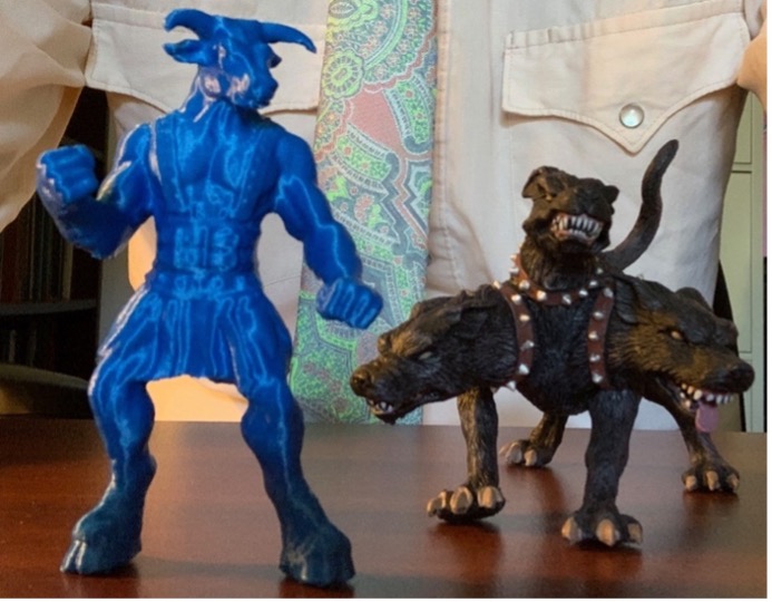 Left, a blue 3D printed figure of a minotaur; Right, a sculpture of Cerberus, a brown dog with three heads and three studded collars baring its teeth