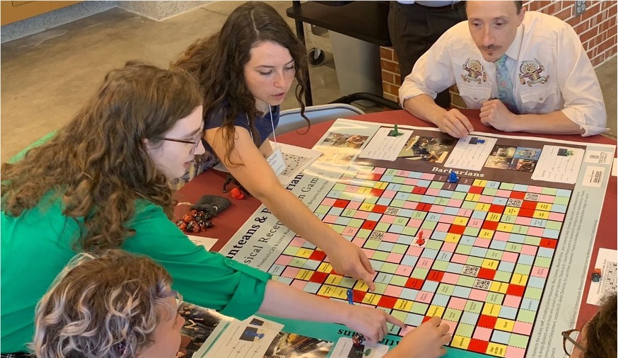 A group of people playing the game on the board in the above image. Two women are reaching their arms across the board.