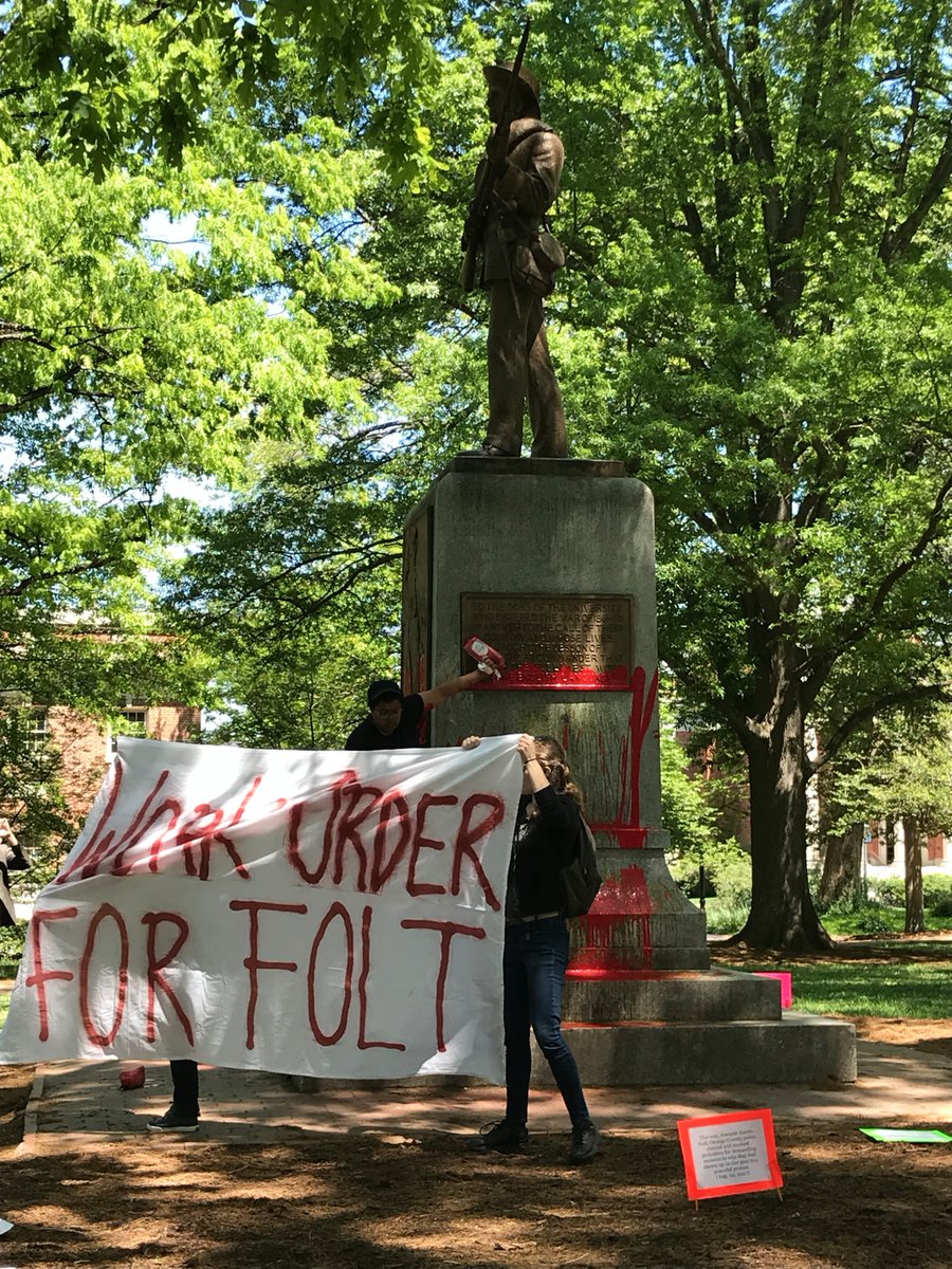 Students hold a sign that read "WORK ORDER FOR FOLT" while Maya Little pours ink and blood on Silent Sam (Image by permission of the Workers Union at UNC-CH).