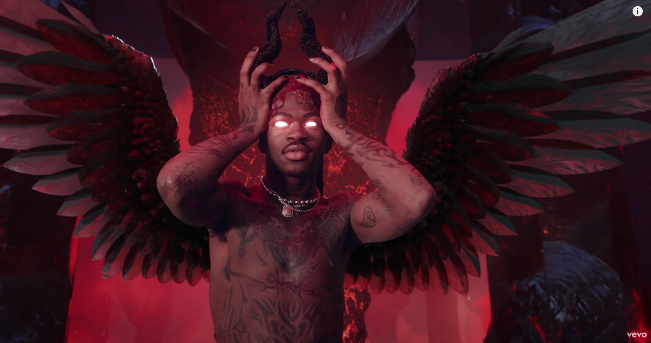 Lil Nas X assumes the role of Satan, colored red with feathered wings and white eyes.