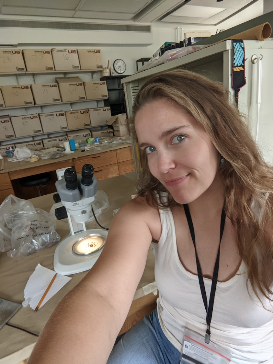 A light-skinned woman with light brown hair takes a selfie in a lab.